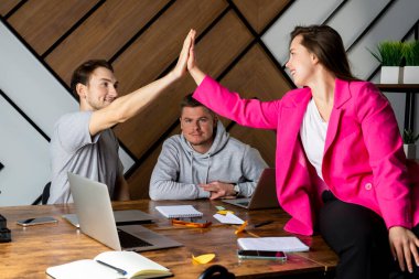 İki meslektaş beşlik çakar, üçüncüsü hiç dikkat çekmeden oturur. Ofiste 