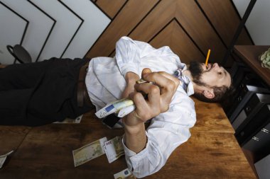 Stresli ve yorgun ofis çalışanı ya da elinde bozuk para ya da banknotlarla bir masada yatan bir iş adamı. Mutluluğu satın al.