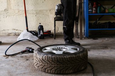 Bir araba tekerleğinde, yanında pnömatik bir ingiliz anahtarı olan bir araba atölyesinde yatıyor..