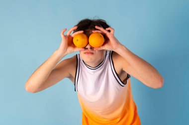 Genç bir adamın oynaşma fotoğrafı. Gözler yerine meyveler kullanırdı. Güneş gözlüğü, gömlek, şort, izole edilmiş mavi renk..