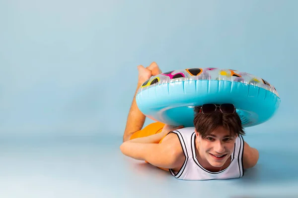 stock image Funny man with blue inflatable swimming circle flaunts his strength on light blue background. Full length of playful strong male swimmer. Summer vacation concept.