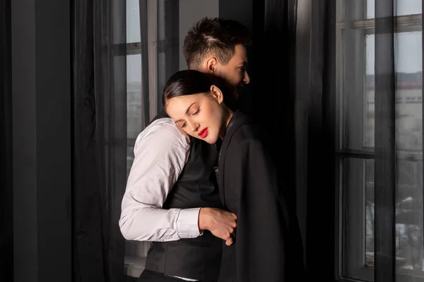 A young elegantly dressed couple in a dark room. The gentleman offers his jacket to the girl so that she does not get cold. Good manners and taking care of a woman.