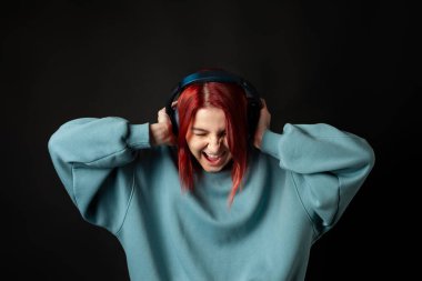 Mavi, büyük kapüşonlu, kulaklıkla müziğin tadını çıkaran çekici, genç, kızıl saçlı kız..