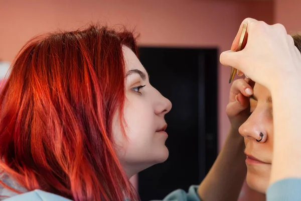 makeup artist or visagiste working on a woman's brows in a studio, plucks the eyebrows.