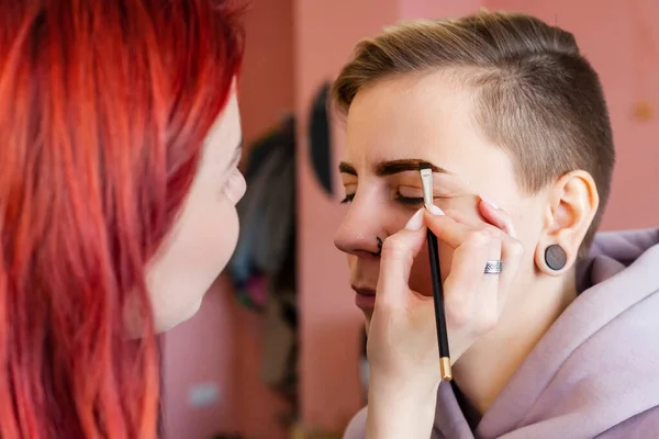 makeup artist or visagiste working on a woman\'s brows in a studio, paints the eyebrows.