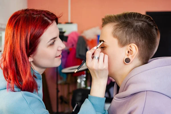 makeup artist or visagiste working on a woman's brows in a studio, paints the eyebrows.