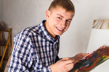 Mutlu gülümseyen ressam ya da sanatçı kareli gömlekli atölyede yeni bir sanat üzerinde çalışıyor..