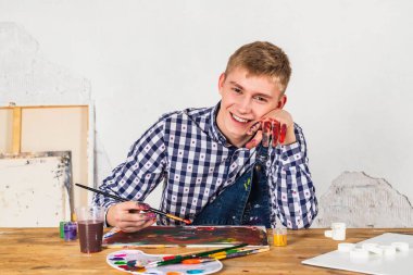 Mutlu gülümseyen ressam ya da sanatçı kareli gömlekli atölyede yeni bir sanat üzerinde çalışıyor..