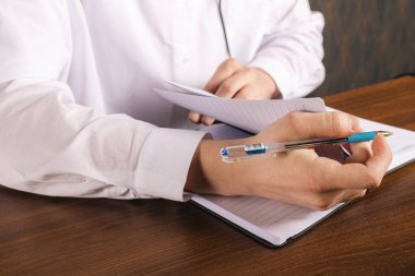 Beyaz gömlekli tanınmayan genç adam masanın yanında oturuyor, not defterine yazıyor ve not alıyor..