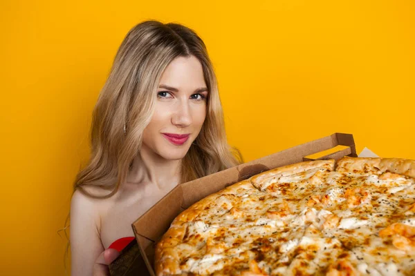 Stock image A beautiful fit young blonde girl with a big open pizza box. Isolated on yellow.