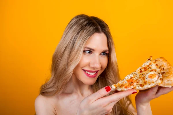 A beautiful fit young blonde girl posing with a pizza slice. Isolated on yellow.