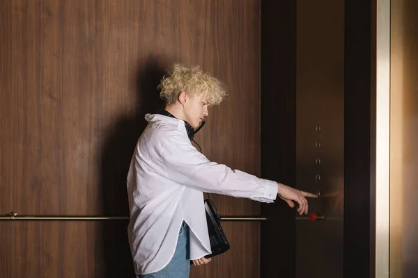 stock image Young trendy teenager, the programmer or IT specialist with a laptop or notebook in hand is pressing a button in an elevator.