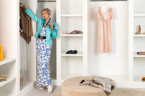 stock image A stylish elderly lady in a dressing room and wardrobe looking for a clothes to wear. Concept of Aging and beauty.