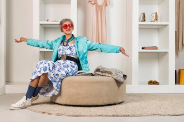 Şık, yaşlı bir bayan soyunma odasında ve gardıropta oturuyor. Yaşlanma ve güzellik kavramı.