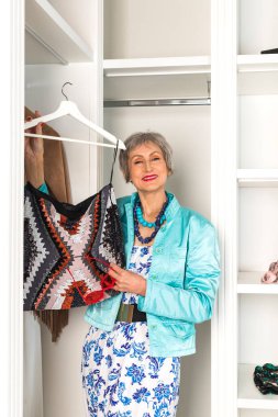 Soyunma odasında şık, yaşlı bir kadın ve giyecek kıyafet arayan bir gardırop. Yaşlanma ve güzellik kavramı.