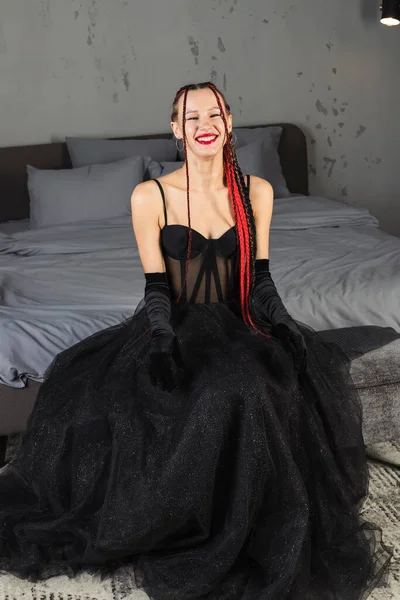 ベッドの上にポーズをとる長い赤の編組を持つスタイリッシュな黒のドレスで優雅な女性 — ストック写真