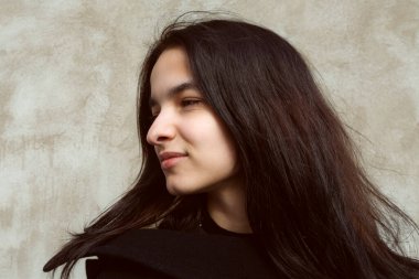 Siyahlar içinde genç bir esmer beton duvara karşı poz veriyor..