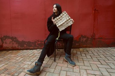 Siyahlar içinde genç bir esmer elinde karton yumurta tepsisiyle sokakta poz veriyor..