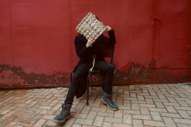 Siyahlar içinde genç bir esmer elinde karton yumurta tepsisiyle sokakta poz veriyor..