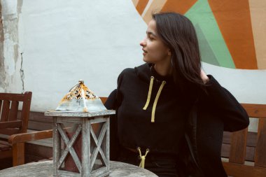 Siyah giyinmiş genç bir esmer elinde fenerle sokakta poz veriyor..