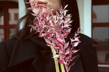 Siyahlar içinde genç bir esmer, elinde pembe yapraklı dekoratif bir dalla sokakta poz veriyor..