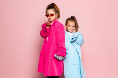 Yetişkinler gibi giyinmiş iki küçük kız. Büyük beden kıyafetler giyen çocuklar. Moda çocukları el ele tutuşuyor. Pembe arka planda izole edilmiş.
