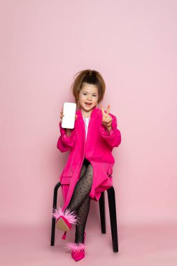 Pembe ceketli küçük bir kız. Yetişkin kıyafetleri giyen ve telefon görüntüsü gösteren bir çocuk. Pembe arka planda izole edilmiş.