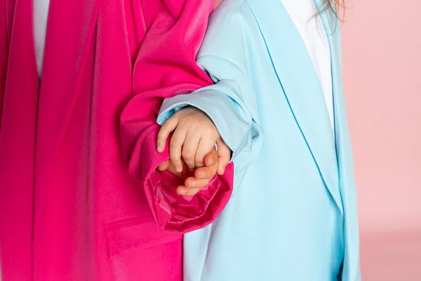 Two little girls are holding hands close-up. Isolated on pink background.