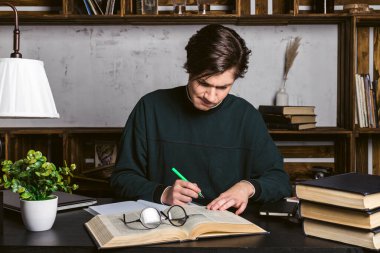 Düzgün giyinmiş, yuvarlak bardaklar içindeki çalışkan genç bir adam, masada oturuyor, öğreniyor ve kitap okuyor..