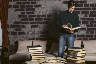 Düzgün giyinmiş, yuvarlak gözlüklü zor öğrenen bir öğrenci yığınlar ve kitap yığınları arasında okuyor ve çalışıyor..