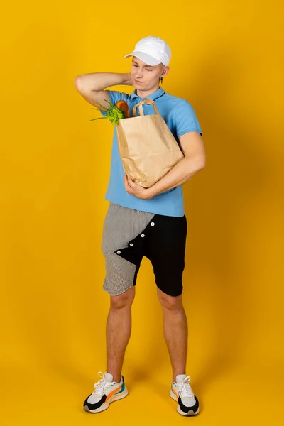Mladý Muž Modrém Tričku Čepici Drží Papírový Sáček Jídlem Izolované — Stock fotografie