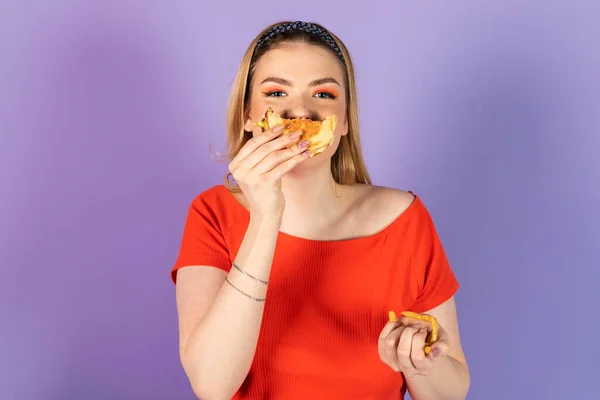 沾满蛋黄酱的血迹斑斑漂亮的女孩吃快餐 便宜的汉堡包 装着芝士汉堡 快餐和不健康的饮食 紫色背景的孤立物 — 图库照片