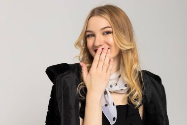 Çekici, mutlu ve gülümseyen kıvırcık saçlı kız zarif giyinmiş, gülüyor ve eliyle ağzını kapatıyor. Pahalı kıyafetler, tarz ve moda konsepti.