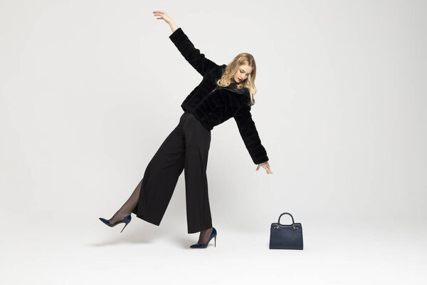 Young Curly blonde girl elegantly dressed, leaning back and reaching her hand to a handbag on the floor. expensive clothes, style and fashion concept.