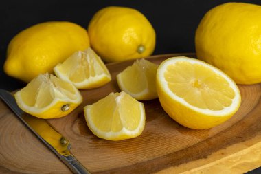 Taze, parlak sarı bir bütün ve ahşap bir kesme tahtasının üzerinde duran limonlar. Siyah, koyu gri arkaplanda izole edilmiş.