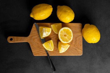 Taze, parlak sarı bir bütün ve ahşap bir kesme tahtasının üzerinde duran limonlar. Siyah, koyu gri arka planda izole edilmiş. Düz yatış, üst manzara. Boşluğu kopyala.