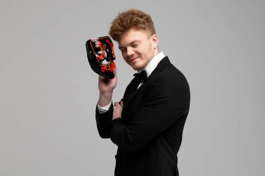 Sivri siyah takım elbiseli şık genç adam elinde parlak bir maske tutuyor. Gizli kimlik ve kişilik. Gizli niyetler. Kimlik değiştirme. Beyaz arkaplanda izole.