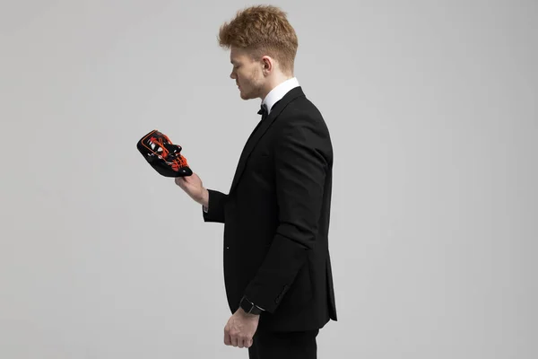 stock image Stylish young man in a sharp black formal suit is holding a bright mask in his hands. Concealed identity and personality. Hidden intentions. Identity substitution. Isolated on white background.