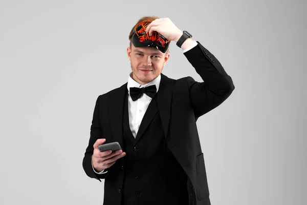 Stylish young man in a sharp black formal suit wearing a bright face mask, holds a phone. Concealed identity and personality. Hidden intentions. Identity substitution. Isolated on white background.
