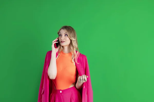 stock image Young curly blonde dressed in pink blazer and pants, talking to the phone, calling, busy thoughtful expression