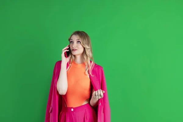 Stock image Young curly blonde dressed in pink blazer and pants, talking to the phone, calling, busy thoughtful expression