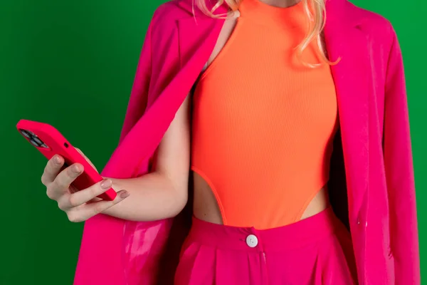stock image Young curly blonde dressed in pink blazer and pants, looking at the phone, no face, close up.