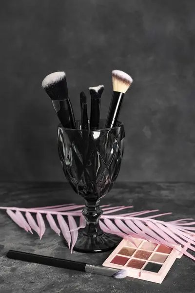 一组化妆刷 化妆品 化妆工具和粉色花卉装饰 分枝和树叶 背景为深灰色斑斑 — 图库照片