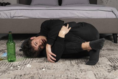 Hapların ve bir şişe alkolün arasında yerde yatan depresif bir adam. Zihinsel sorunları olan genç bir adam. alkol ve uyuşturucu bağımlılığı.