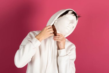 Beyaz kapüşonlu, maskeli şüpheli bir gencin portresi. Gizli hayran, gizli kimlik konsepti. Pembe arka planda izole edilmiş.