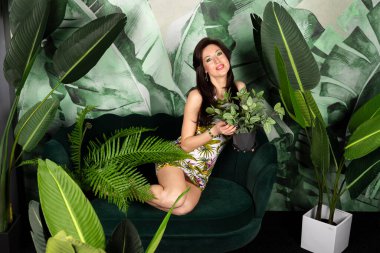 Çiçeklerin tadını çıkaran taze yeşil makyajlı güzel esmer kadın büyük tropikal yapraklarla bitkilerin arasında poz veriyor. Doğa kavramına saygı göstermek..