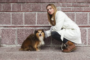 Sarışın genç bir kız ve minyatür köpeği, sokakta yürüyorlar, uzun adımlarla ayakta duruyorlar..