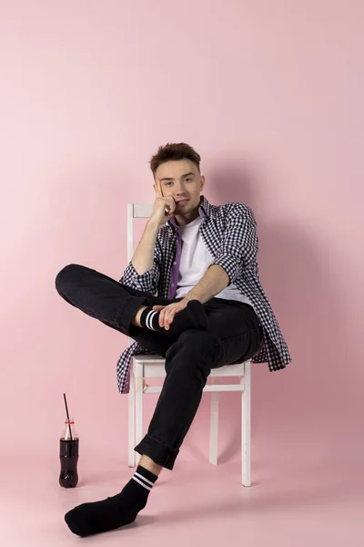 A happy young man sitting with a bottle of coke. fast food and sugar addiction. Isolated on pink background.