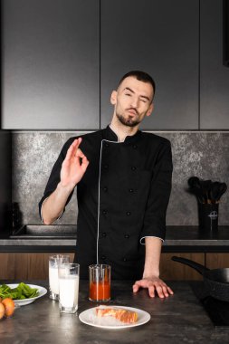 Mutfakta siyah üniformalı bir aşçının portresi. Kahvaltı hazırlamak için malzemelerle birlikte..