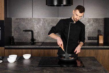 Mutfakta siyah üniformalı bir aşçı yemek pişiriyor.